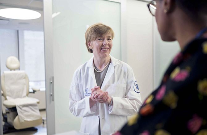 Doctor in a white coat smiles, speaking to another person in a medical office.