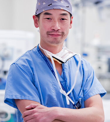 An MSK clinician wearing light blue surgical scrubs standing in an operating room, smiling. 