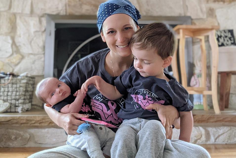 Woman wearing a blue bandana holding her newborn baby and toddler on her lap 