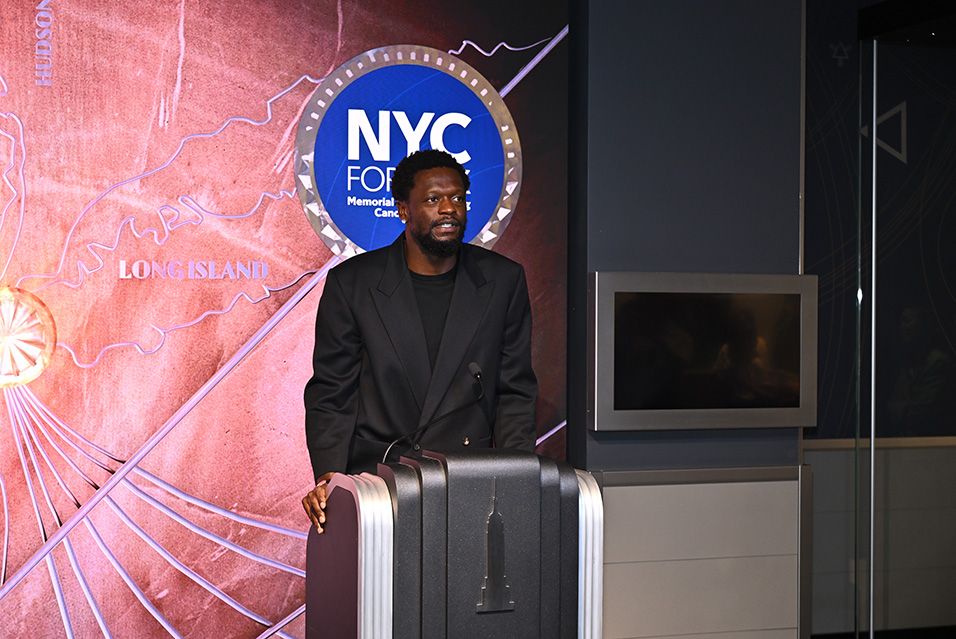 A tall man stands at a podium, with an NYC for MSK sign projected on the wall behind him. 