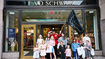 A group of children standing with a person dressed as a toy soldier in front of FAO Schwarz in New York City.